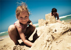 A little girl enjoying a SmarTravel Vacation on the beach buildnig a Sand Castle